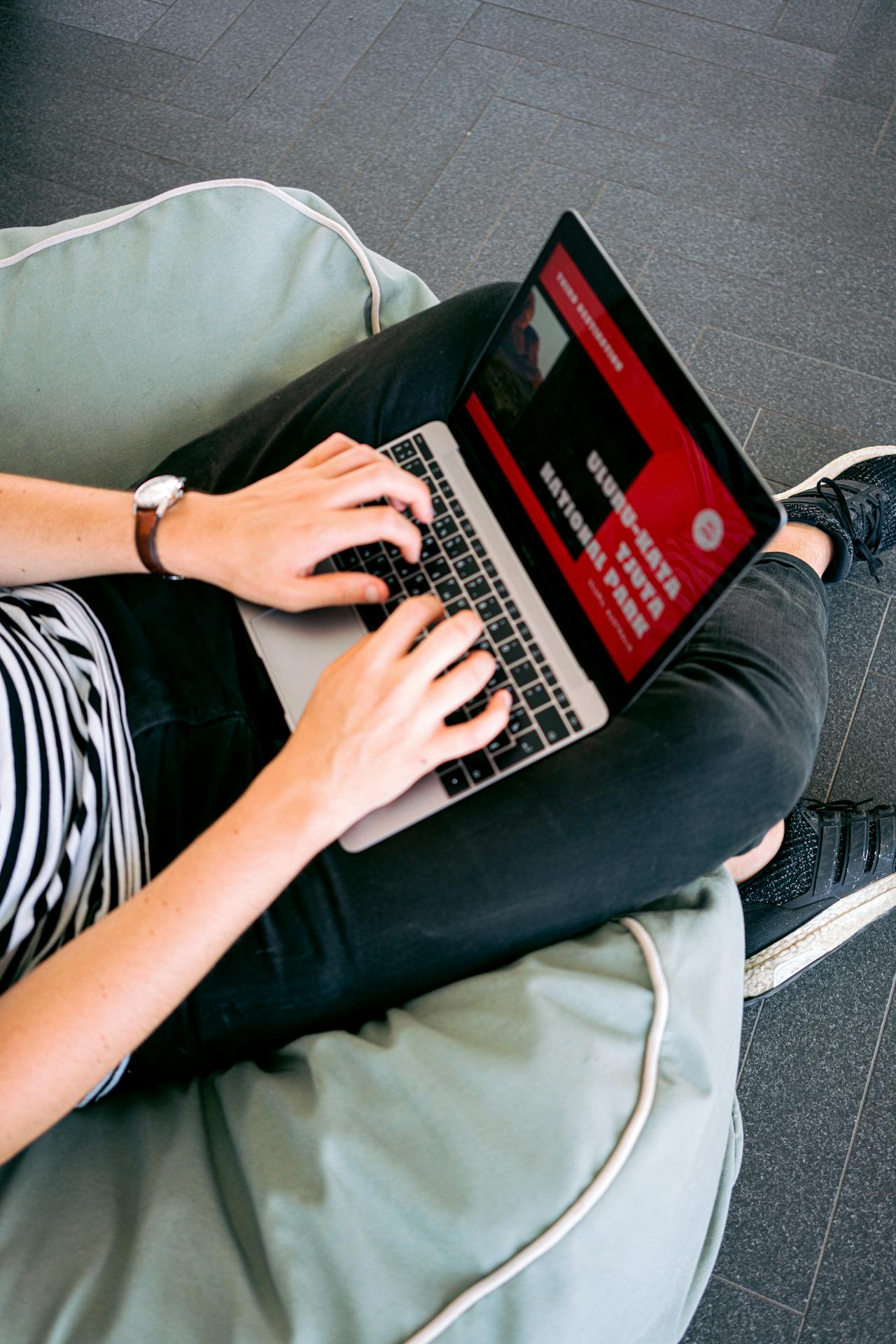 Person sitting on a green bean bag, typing on a laptop